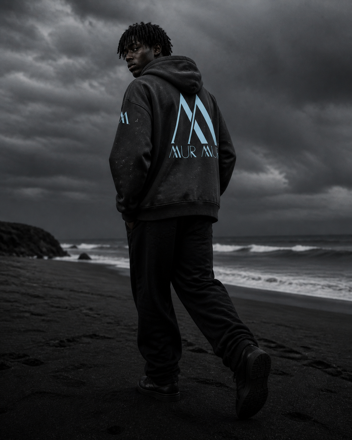 Back view of the washed-black Mur Mur hoodie on the coast