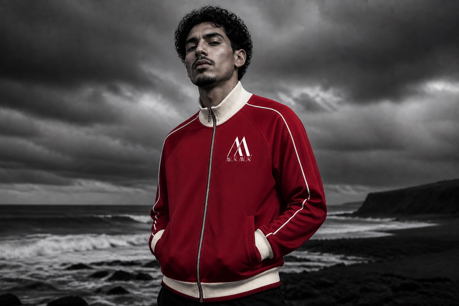 Model wearing the red and cream unisex Mur Mur track jacket on a stormy coast