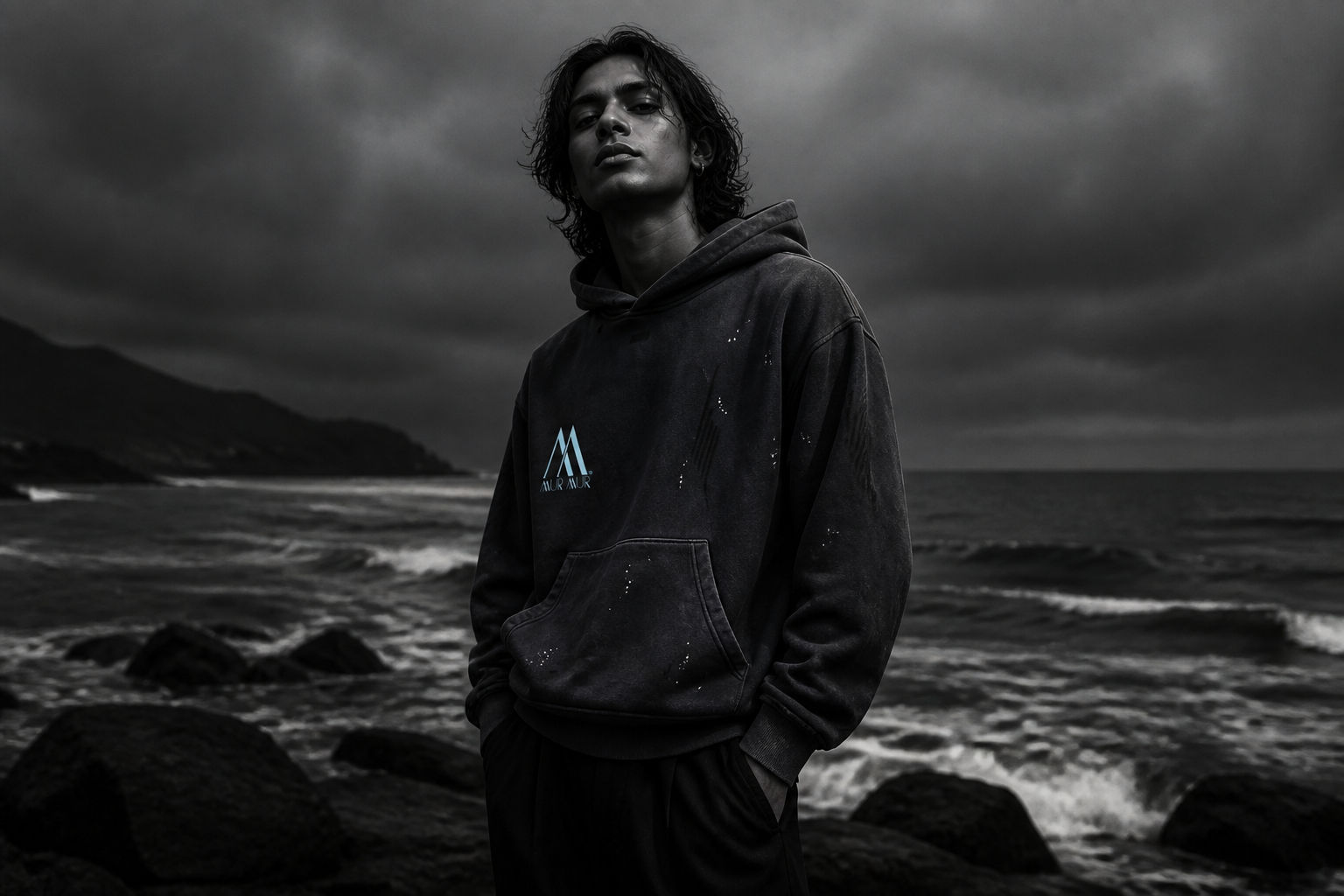 Model wearing the unisex washed-black Mur Mur hoodie on a dark coast