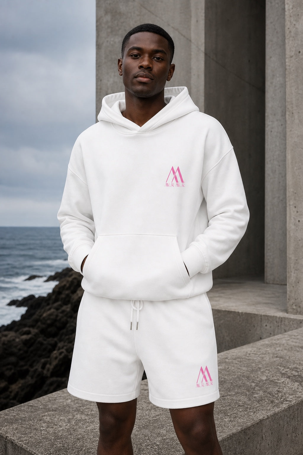 Black male model wearing the Lucent White Mur Mur Hidden-Pocket Heavyweight Hoodie and matching Essential Heavyweight Fleece Shorts, both with pink logos